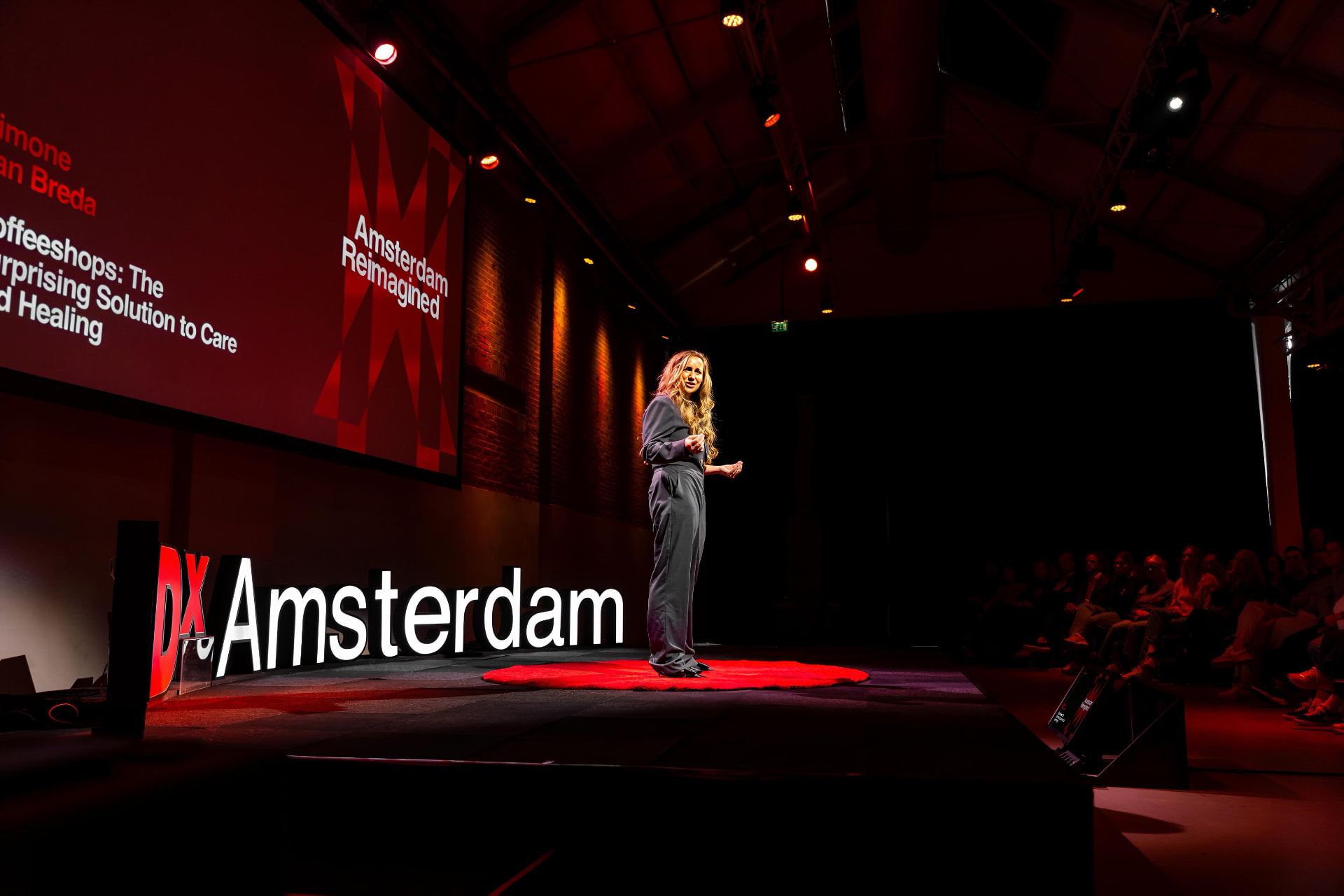 Simone van Breda spreekt op het podium van TEDx Amsterdam, met op het scherm de titel van haar talk
